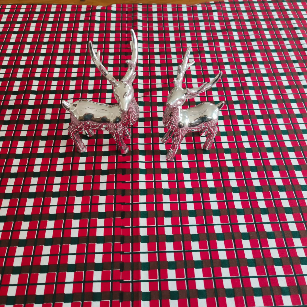 Two silver deer figurines on a red and green checkered fabric