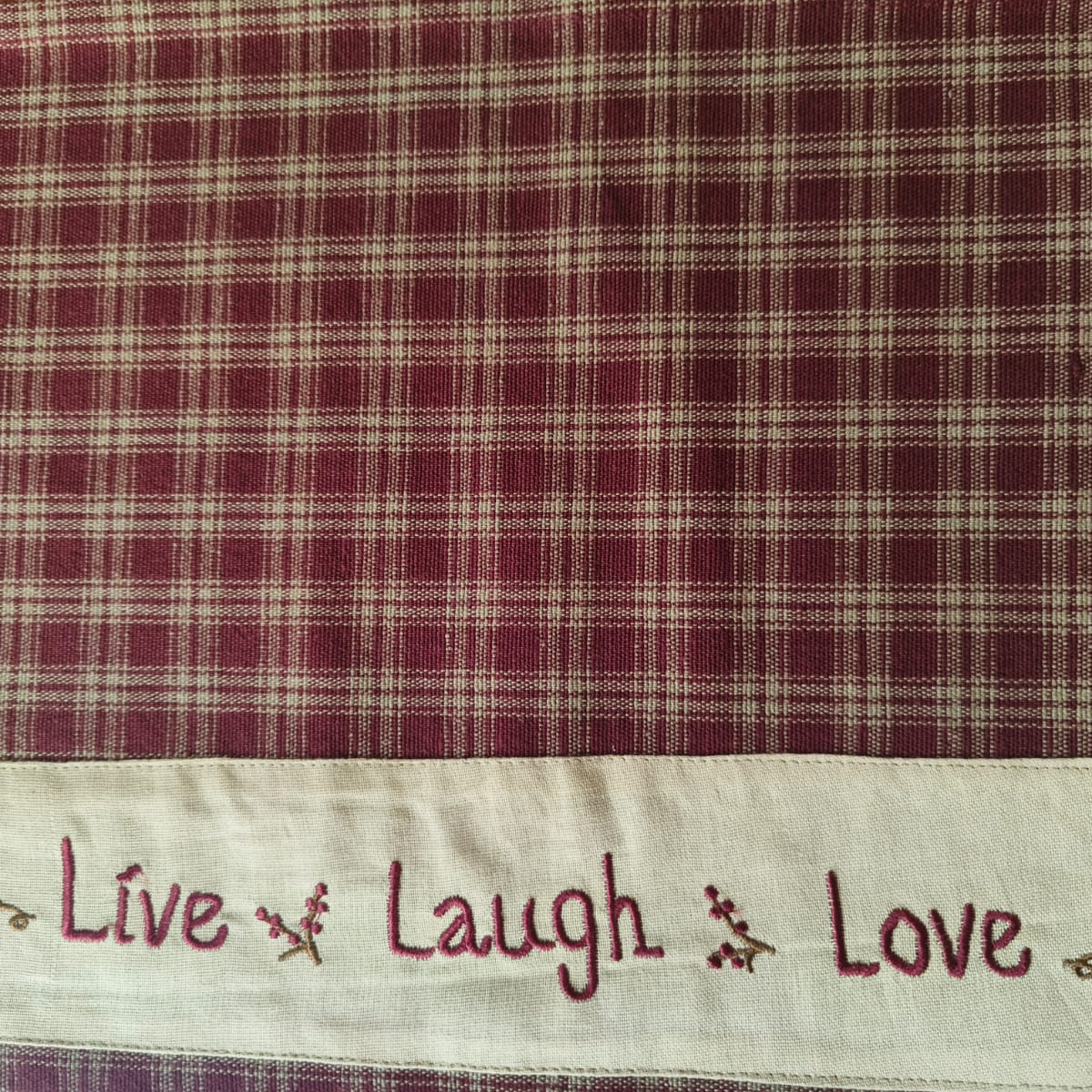 Fabric with plaid pattern and embroidered text 'Live Laugh Love' on a white background